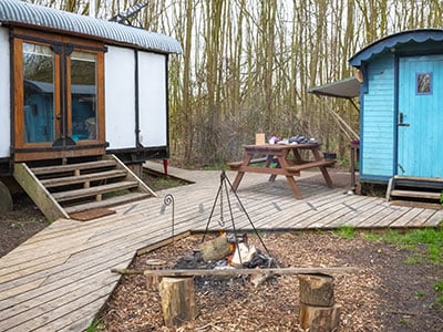 White tiny home by blue tiny home with picnic table and fire pit